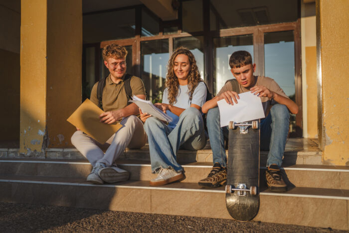 Students Comparing Grades After Exam Results Sitting On School Steps